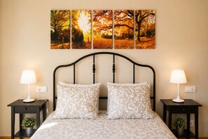 A bed with a white patterned bedspread, two matching pillows, and two bedside tables with lamps. Above the bed is a wall-mounted artwork depicting autumn trees. - Villa Playa de Barro with garden - Llanes (Llanes)