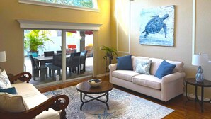 Un salon comprenant un canapé, une table basse et une grande fenêtre donnant sur un espace extérieur aménagé avec des sièges.
