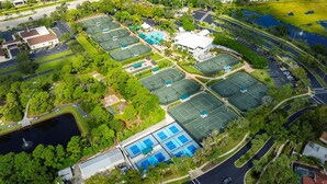 Vue aérienne d’un complexe sportif comprenant plusieurs courts de tennis, une piscine et un parking.