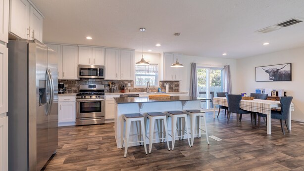 A modern kitchen with stainless steel appliances, a central island with bar stools, and a dining area with a table and chairs. - The Salsbury Star- large family home, downtown location, pet friendly (Cody)
