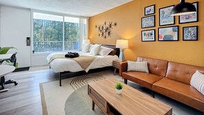 A modern bedroom with a large bed, a brown leather sofa, and a desk. - Cozy King Studio | Zoo, DT & Jacksonville U (Jacksonville)