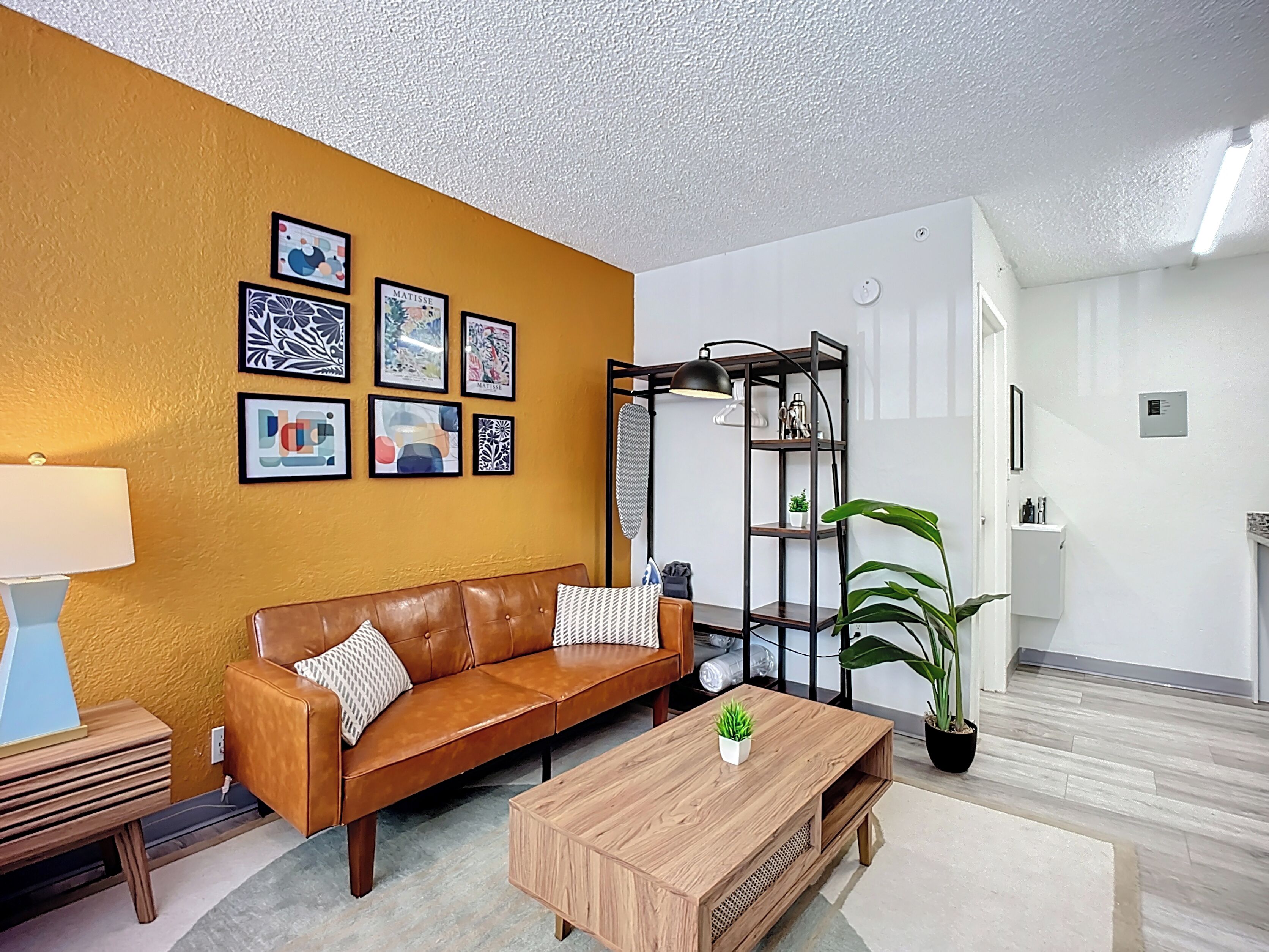 A modern living room with a brown leather sofa, a wooden coffee table, and a black metal shelving unit with a lamp.