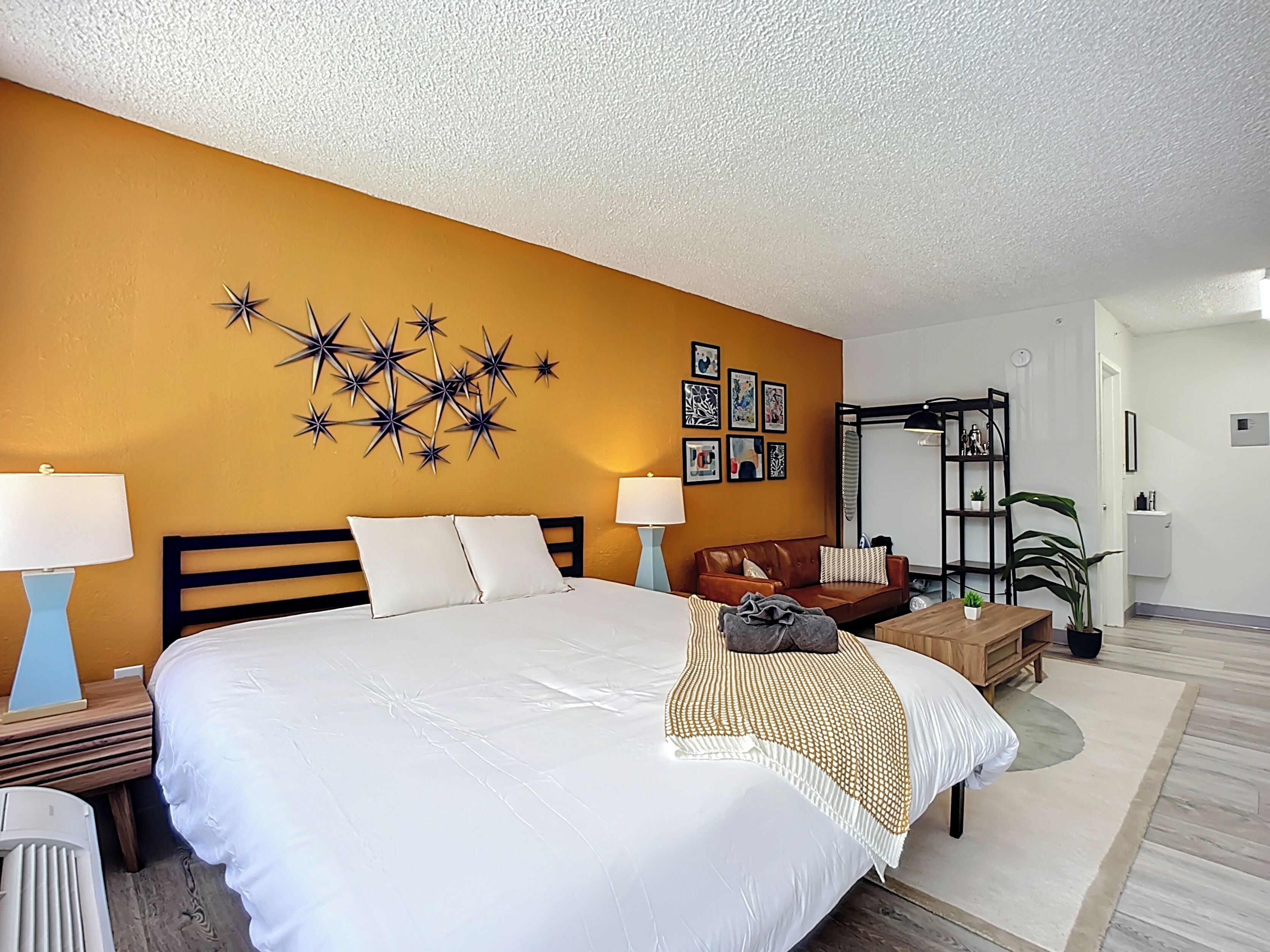 Una habitación de hotel con una cama grande, un cabecero de madera, un adorno en forma de estrella en la pared, un sofá de cuero marrón, una mesa de centro de madera y una pequeña planta en maceta.