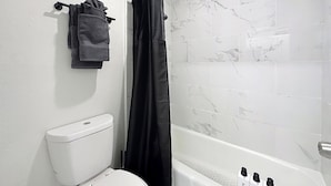 A bathroom with a toilet, a shower curtain, and a tiled wall. - Cozy King Studio | Zoo, DT & Jacksonville U (Jacksonville)