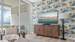 Un soggiorno moderno con un grande televisore, un mobiletto in legno e vista mare tramite una porta in vetro.