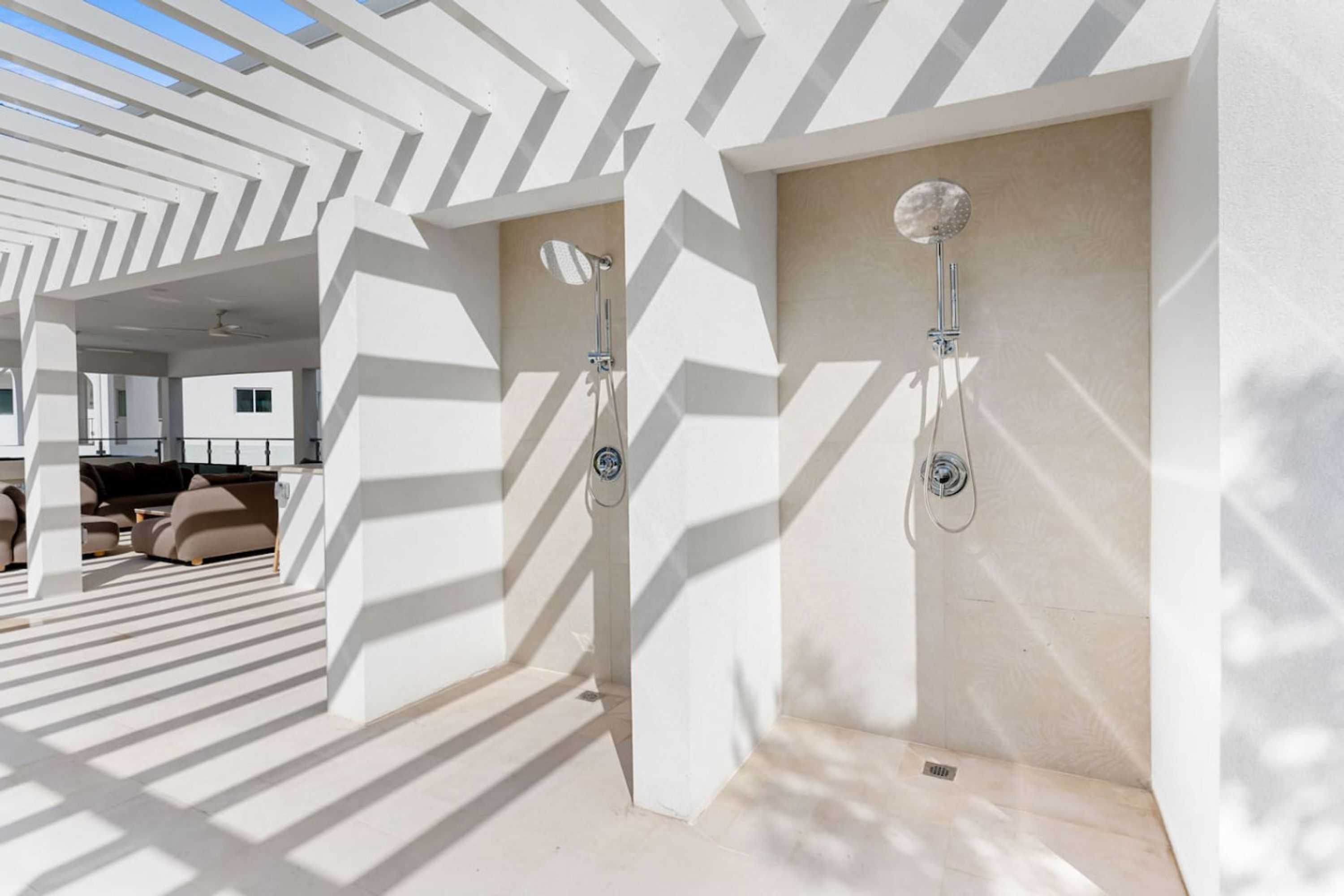 Un área de ducha exterior moderna con diseños geométricos en las paredes y una zona de estar con sofás.