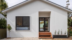 Un bâtiment moderne de plain-pied, avec une façade blanche, une grande fenêtre et une porte vitrée donnant sur une entrée abritée.