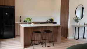Une cuisine moderne dotée d’un îlot central, de deux tabourets de bar, d’un réfrigérateur noir et d’une petite table agrémentée d’un miroir et de plantes.