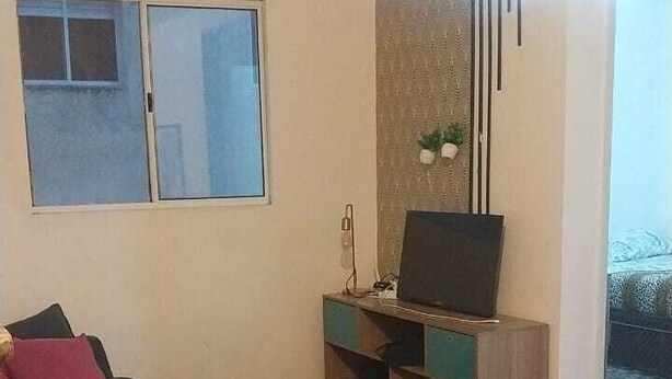 A living room with a sofa, a flat-screen TV on a wooden stand, a patterned wall, and a large window. - APTO Granja Vianna Brand New (Cotia)