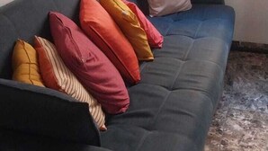A dark blue sofa with multiple cushions in various colors, a white pillow, and a wall-mounted abstract artwork. - APTO Granja Vianna Brand New (Cotia)