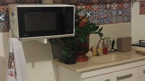 A kitchen with a microwave, cabinets, a sink, and a tiled backsplash. - APTO Granja Vianna Brand New (Cotia)