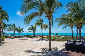 A beach with palm trees, a sandy area, and a wooden deck with a sofa.