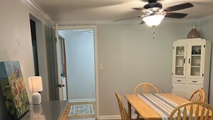 A dining area with a wooden table, chairs, and a red rug. There is a cabinet with glass doors and a ceiling fan above.