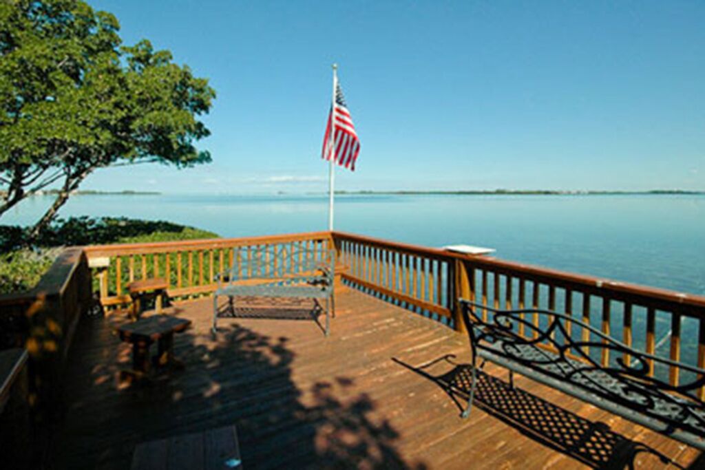 A wooden deck with a railing, a flagpole with an American flag, and a bench.
