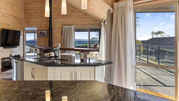Una cocina moderna con una isla central, techo de madera y ventanas amplias que ofrecen vistas al exterior.