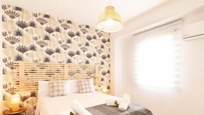 Een slaapkamer met een bed, een nachtkastje met een lamp, een muur met een bladmotief en een raam met jaloezieën.
