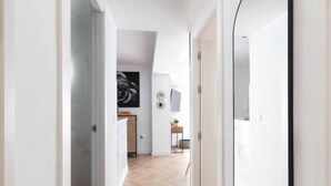 Een gang met een houten vloer, witte muren en een deur die naar een kamer leidt.