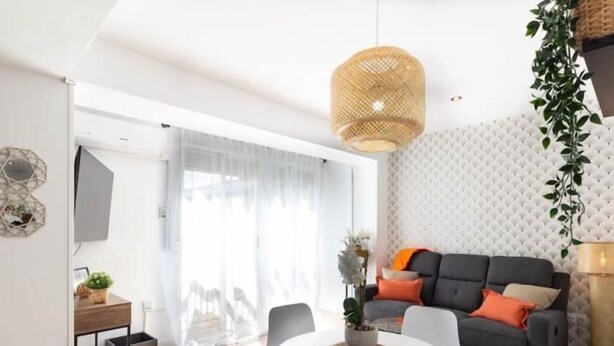 Een moderne woonkamer met een grijze bank, witte stoelen, een ronde witte tafel en een hangende rieten lamp.
