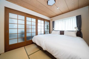 A hotel room with a large bed, sliding glass doors, a window with curtains, and a wooden ceiling. - CRAFT (Asahikawa)