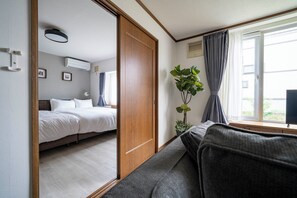 A modern bedroom with a wooden wardrobe, a sofa, a bedside table, a potted plant, and a window with curtains. - CRAFT (Asahikawa)