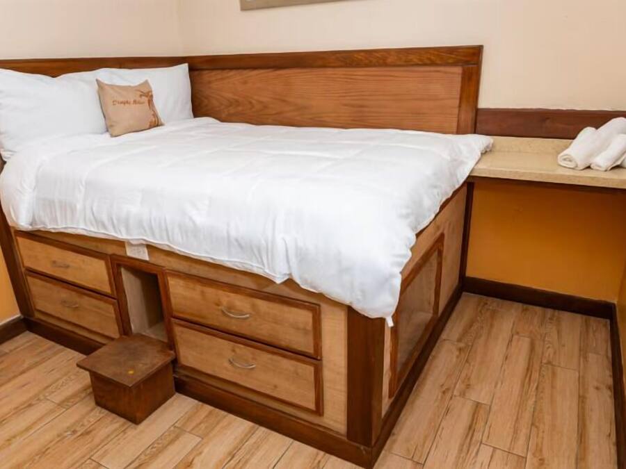 Un lit simple avec une tête de lit en bois, une table de chevet avec un téléphone et une petite table de nuit en bois.