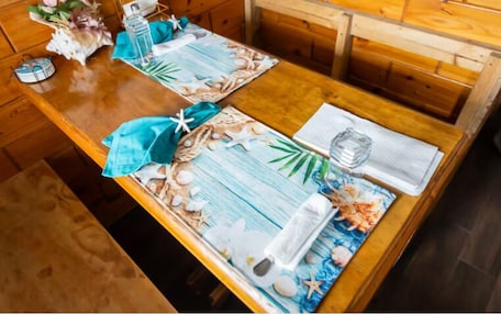 A wooden dining table with a floral table runner, a glass of water, a napkin, and a menu.