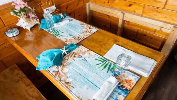 Ett matbord i trä med en blommig bordslöpare, ett glas vatten, en servett och en meny.