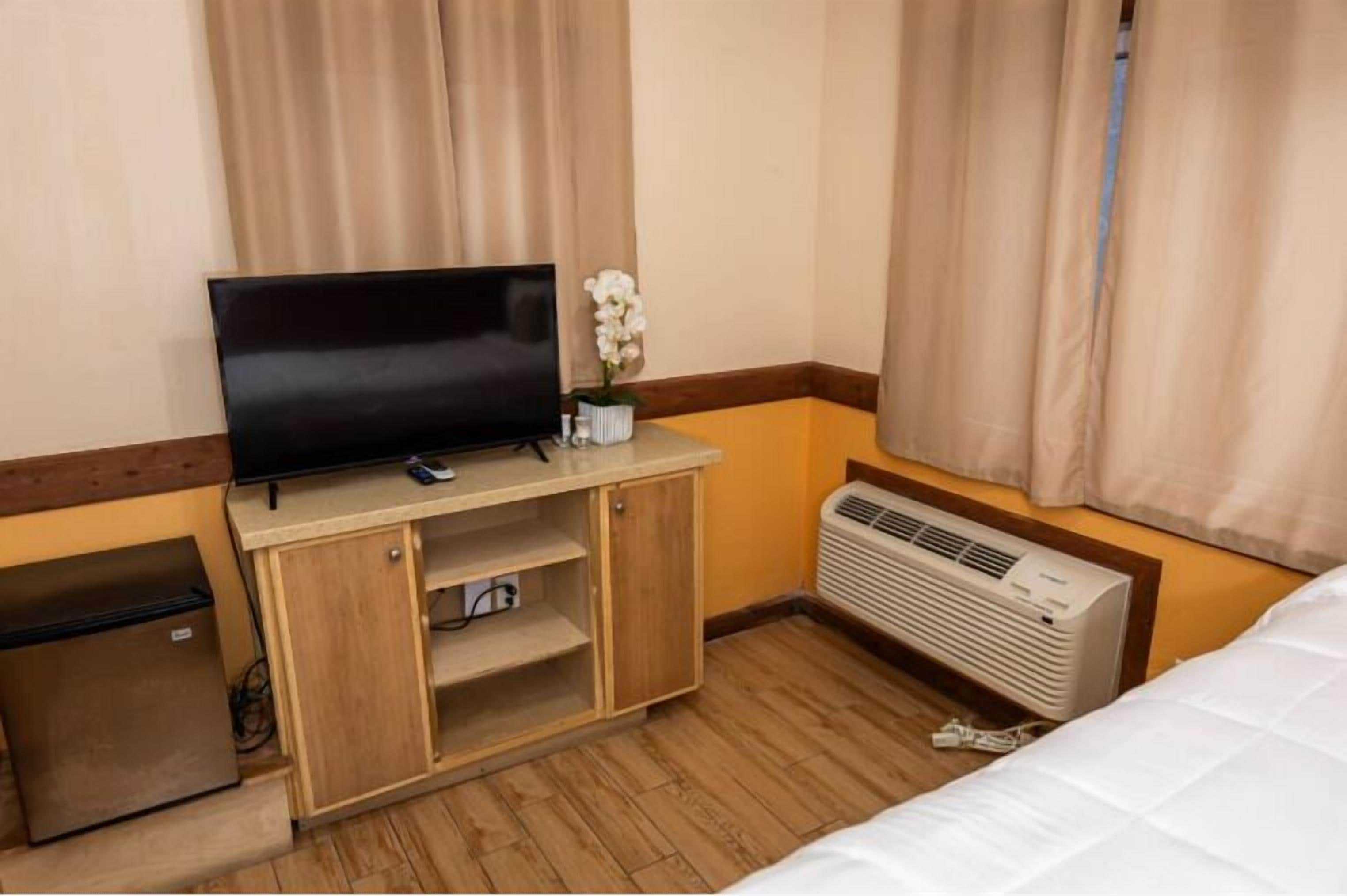 Een hotelkamer met een bed, een televisie op een houten kast, een kleine koelkast en een airconditioner.
