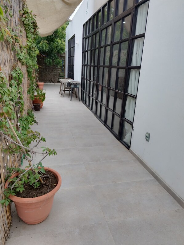 A covered outdoor area with a concrete floor, potted plants, a table, and chairs. - Casa Mango Departamento amplio (Ciudad Fernández)