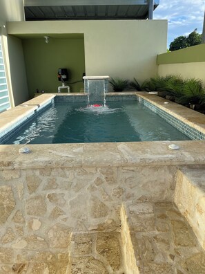 A swimming pool with a waterfall feature, surrounded by stone tiles and potted plants. - Villa Carmin I Apt with Private Pool (Aguadilla)
