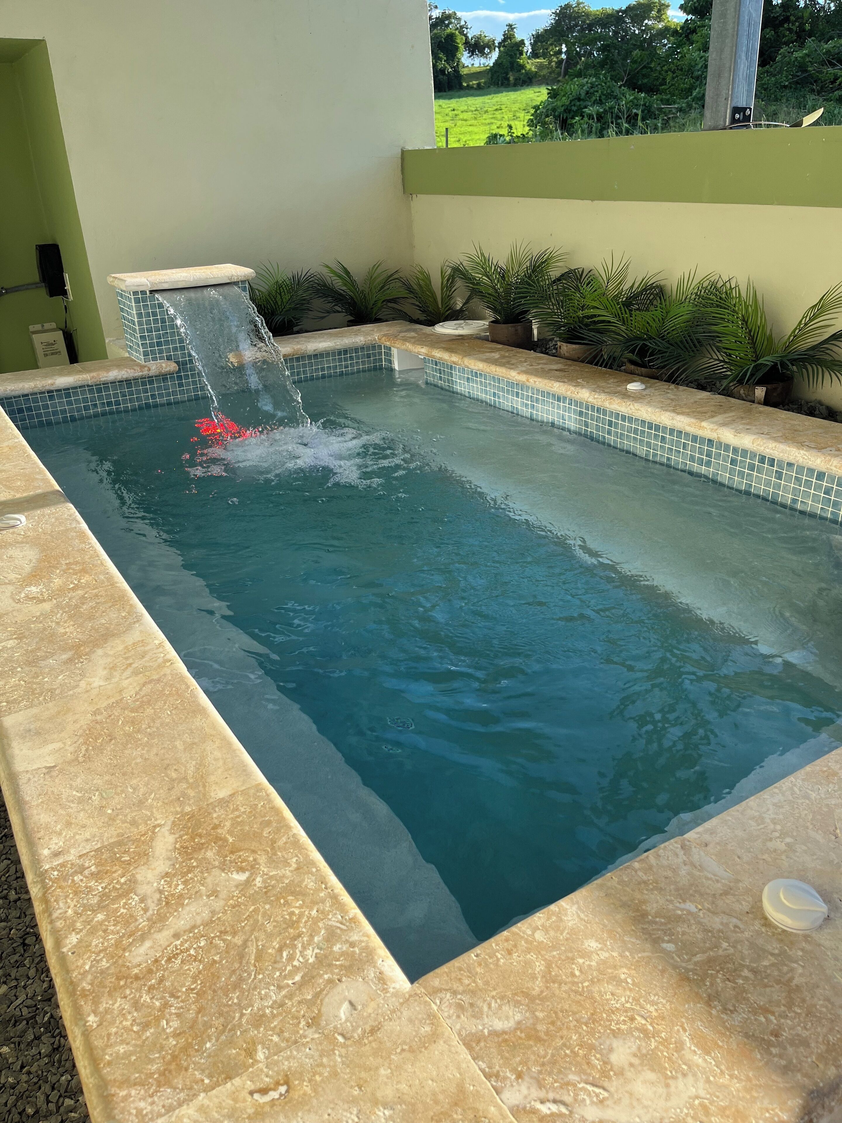 A rectangular pool with a waterfall feature, surrounded by a tiled edge and potted plants.