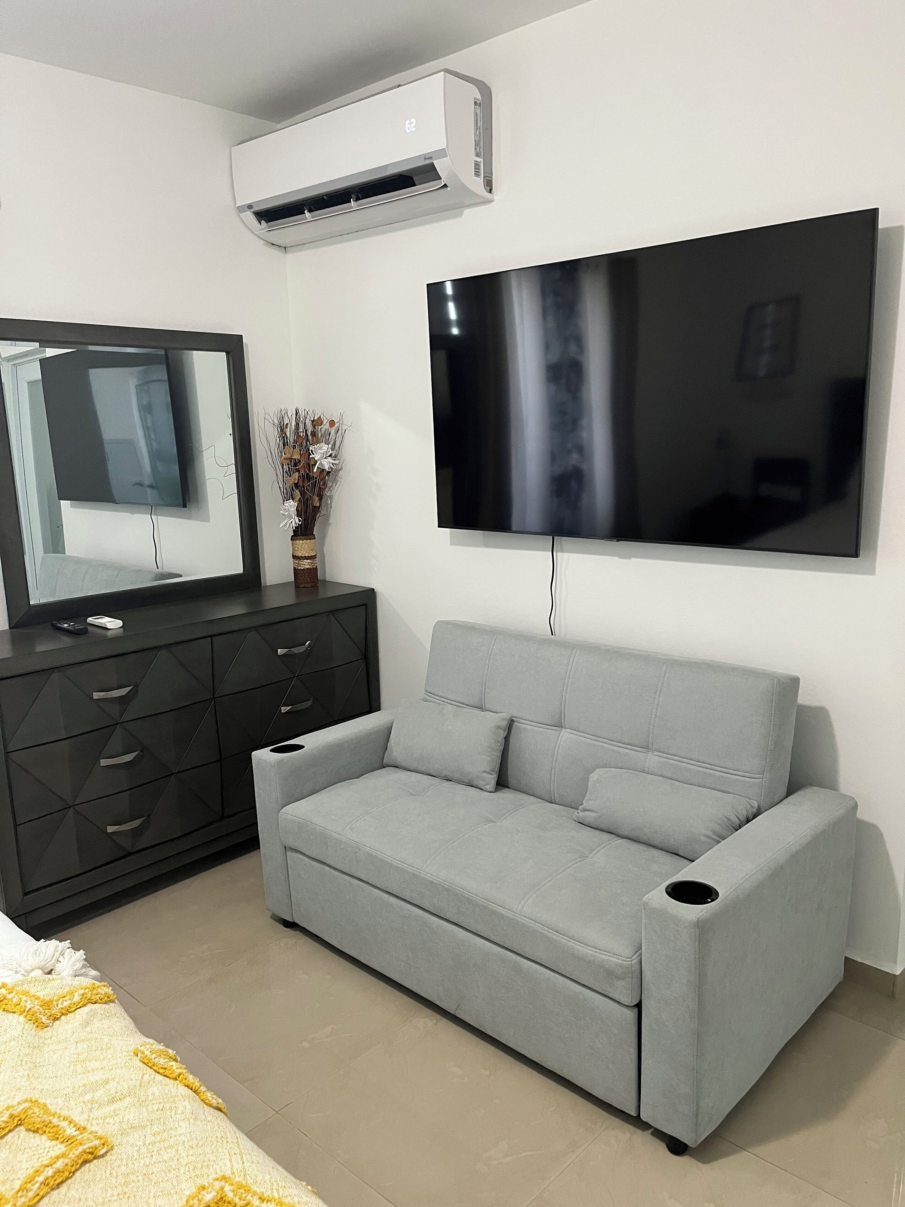A modern living room with a grey sofa, a black TV stand, and a mounted TV.