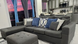 A modern living room with a grey sectional sofa, a matching ottoman, and a patterned rug.