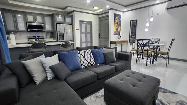 A modern living room with a sectional sofa, ottoman, and dining area with chairs and a table.