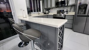 A modern kitchen with a bar area, stainless steel appliances, and a window with blinds.
