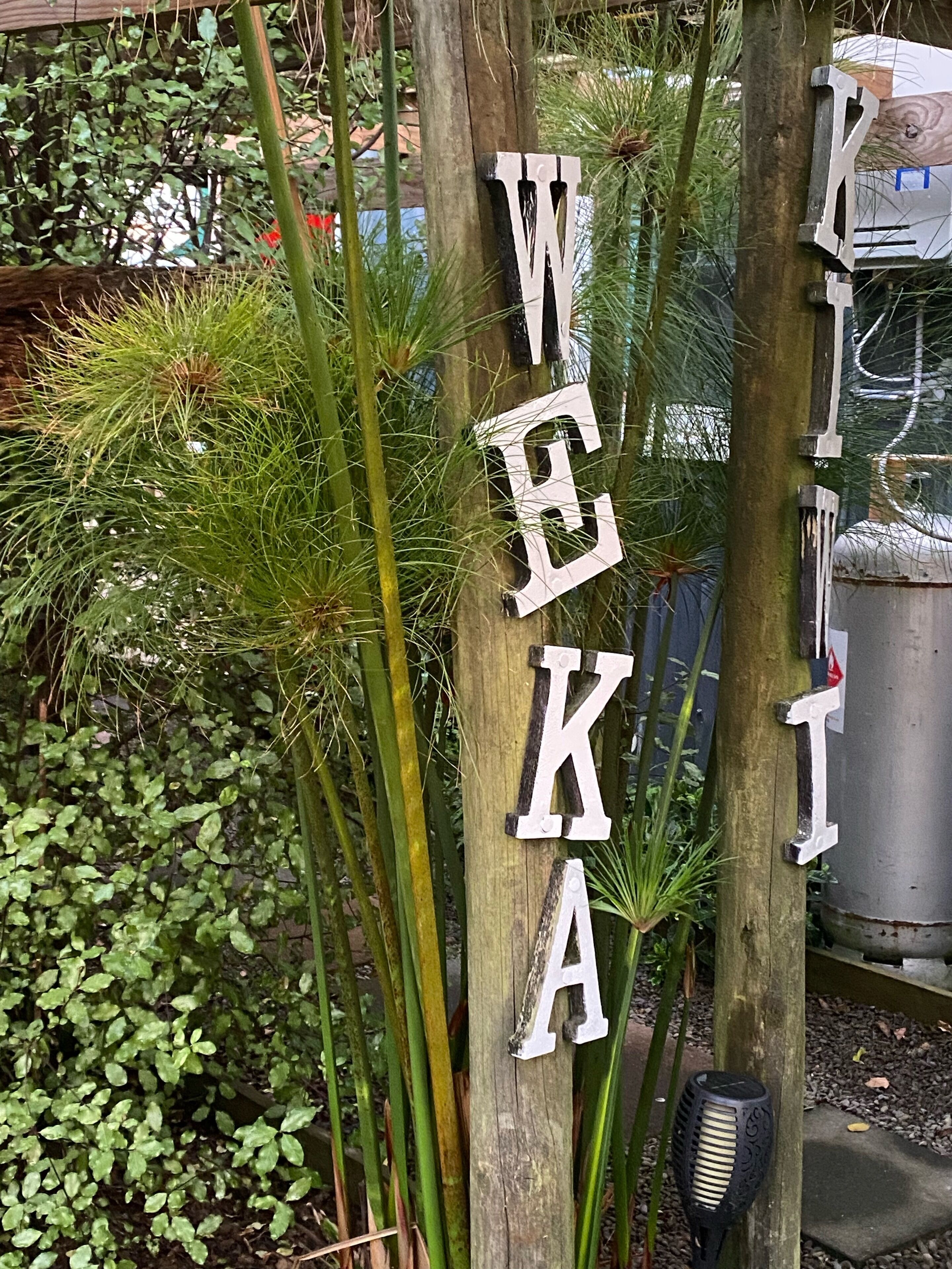 A wooden post with letters spelling "WEKA" and a black decorative item attached to it.