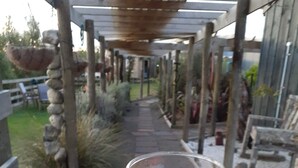 A hand holding a glass of amber liquid, with a stone pathway and wooden structures in the background. - Weka cabin, great views (Wainui)