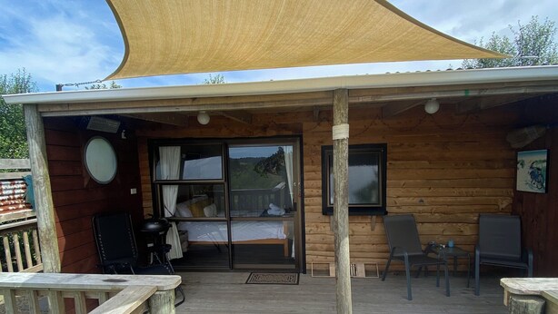 A wooden cabin with a covered deck, a large window, and a white bathtub. - Weka cabin, great views (Wainui)