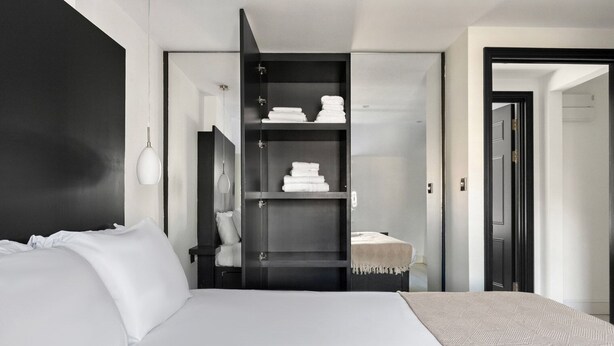 Ein modernes Hotelzimmer mit einem großen Bett, einer eingebauten Garderobe mit Regalen und einem begehbaren Kleiderschrank.