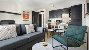 Ein modernes Wohnzimmer mit einem grauen Sofa, einem grünen Sessel und einem Essbereich mit einem Holztisch und Stühlen.