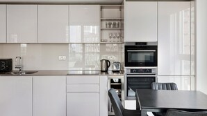 Una cocina moderna con armarios blancos, horno integrado, cafetera y un comedor con mesa y sillas.