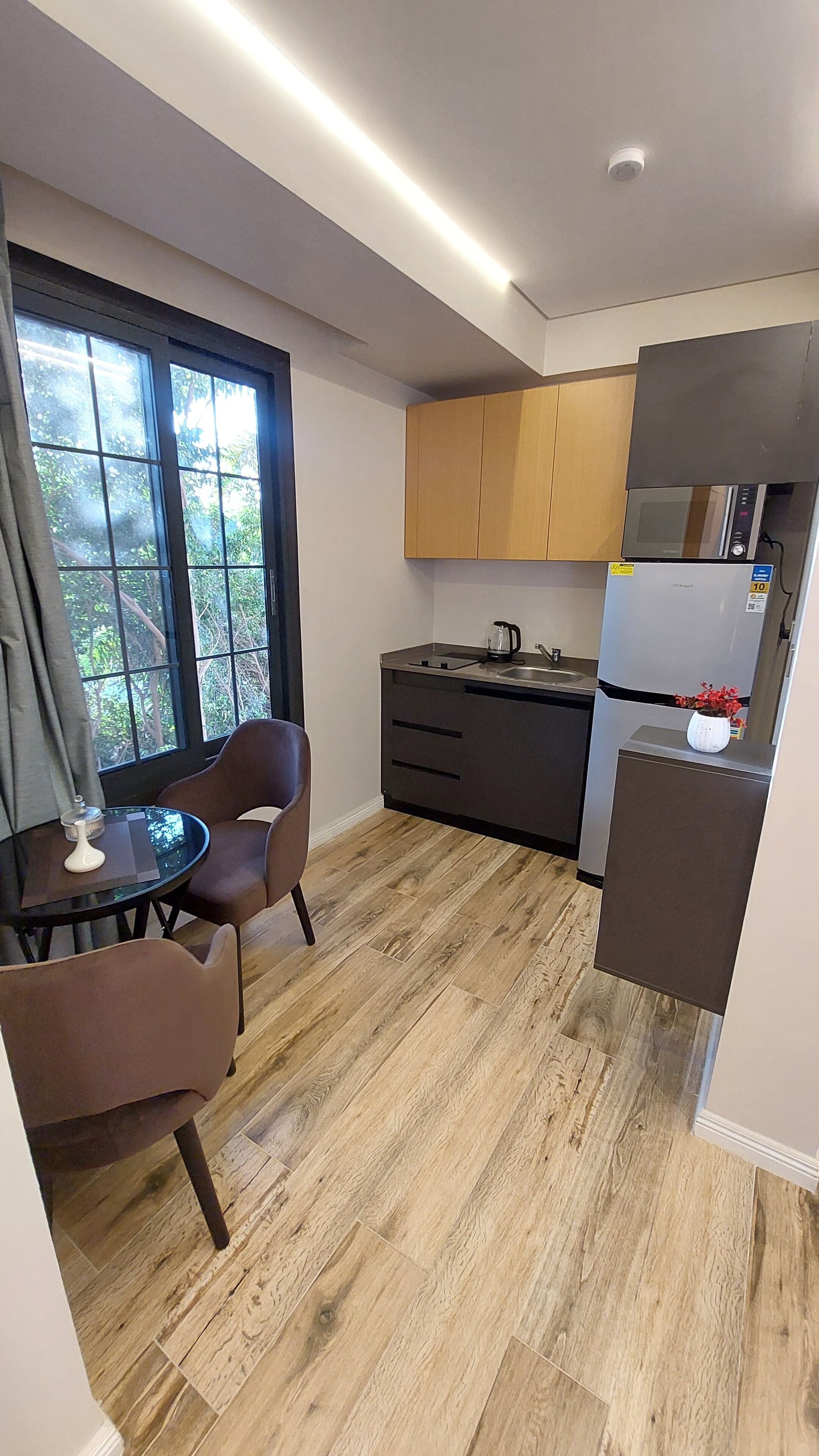 A compact kitchen with wooden cabinets, a microwave, and a sink. There is a dining area with a table and chairs.
