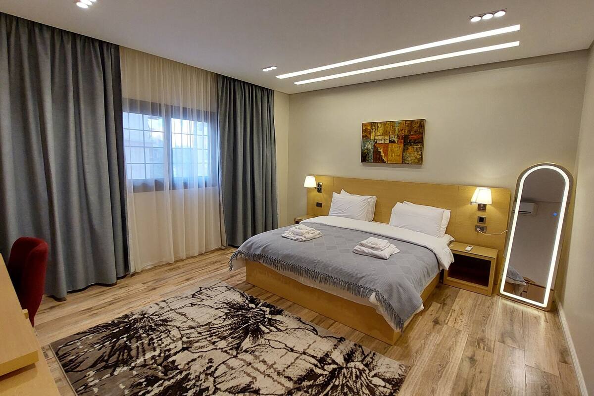 Una camera d'albergo con un letto, una scrivania, una sedia, uno specchio grande e un quadro appeso al muro.