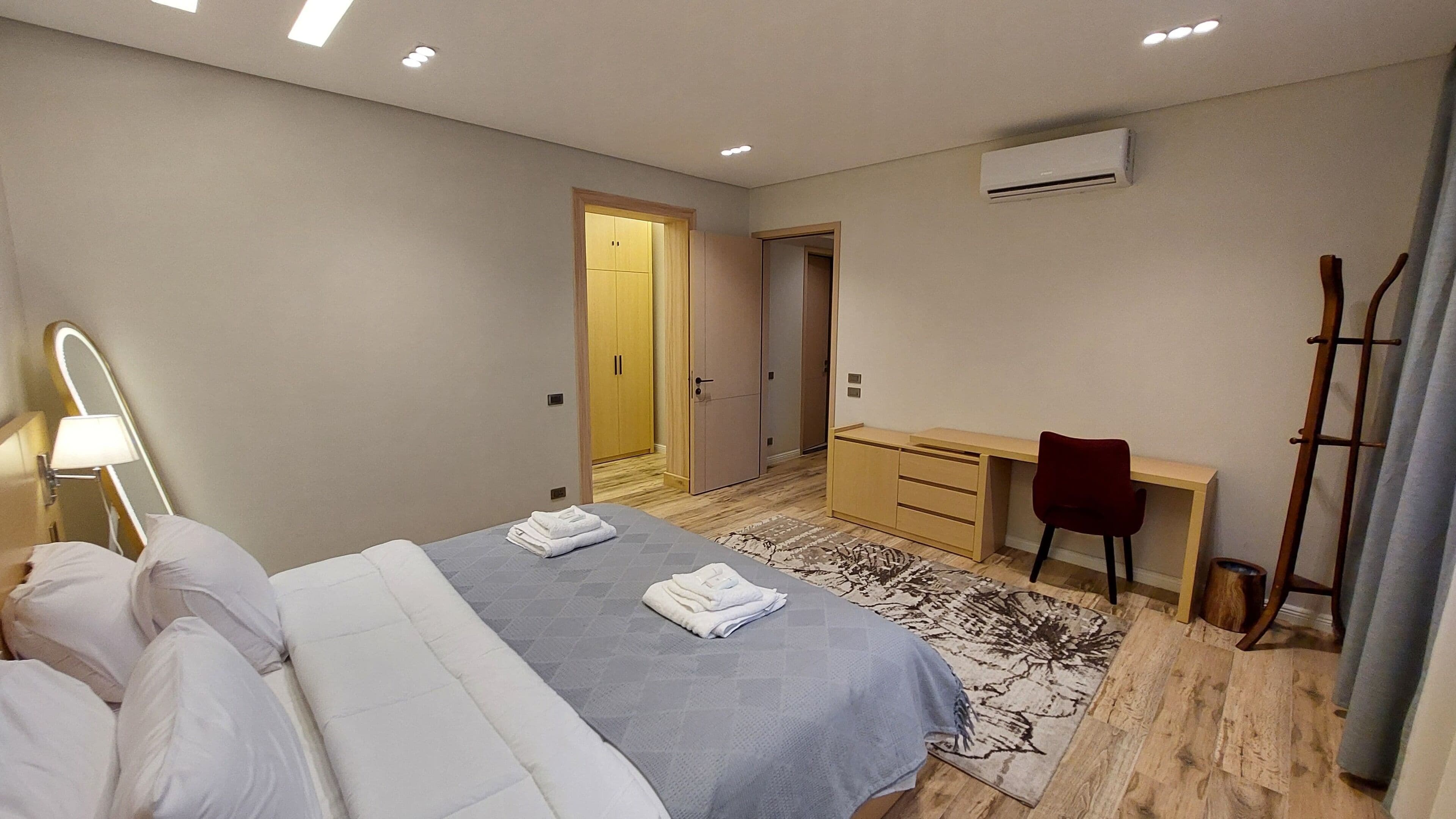 A hotel room with a bed, a desk, a chair, a wardrobe, and an air conditioning unit.