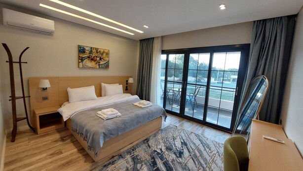 A modern hotel room with a large bed, a desk, a chair, a balcony with a view, and an air conditioning unit. - Mirage Taiaa Hotel Apartments (New Cairo)
