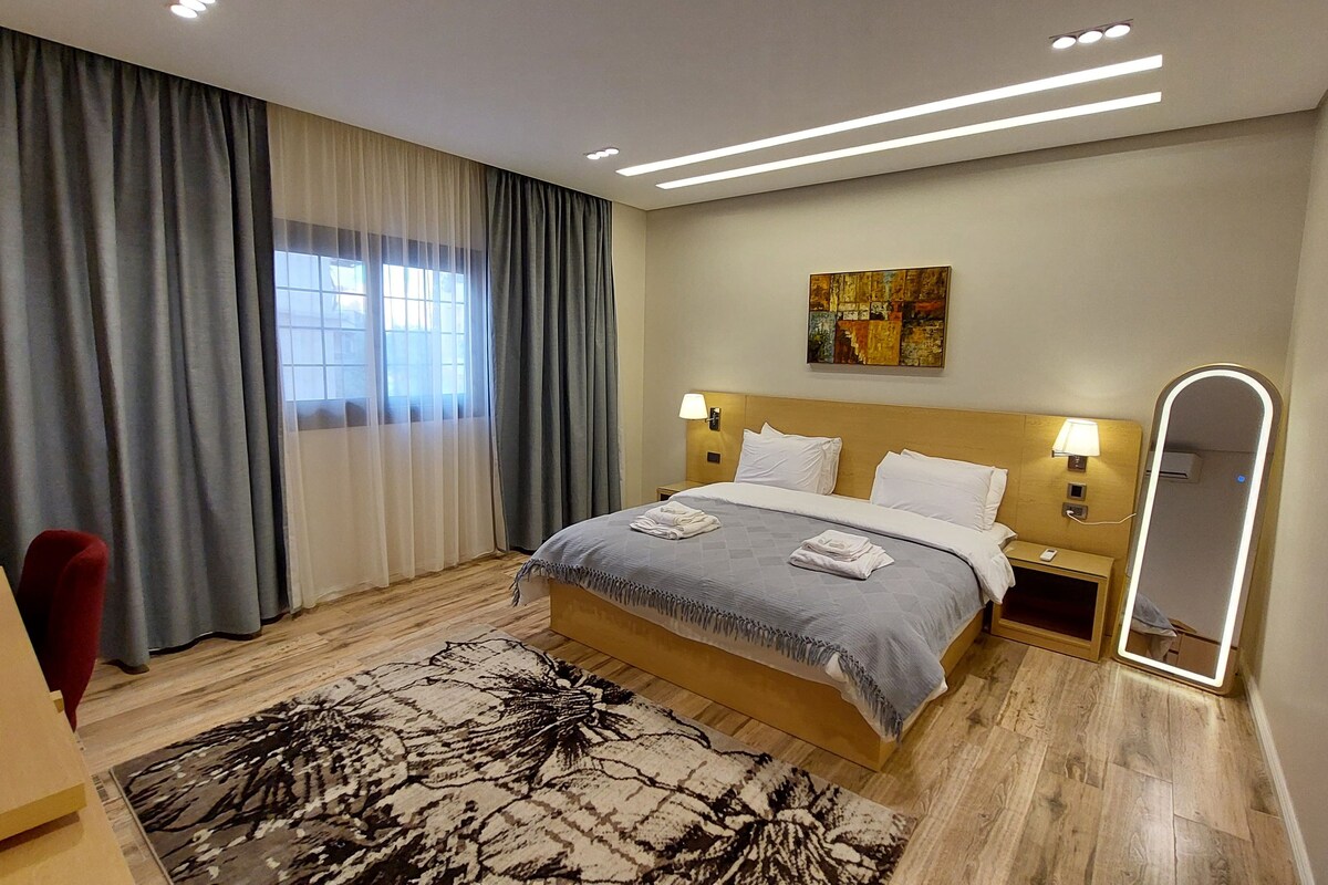 A hotel room with a bed, a desk, a chair, a large mirror, and a painting on the wall.