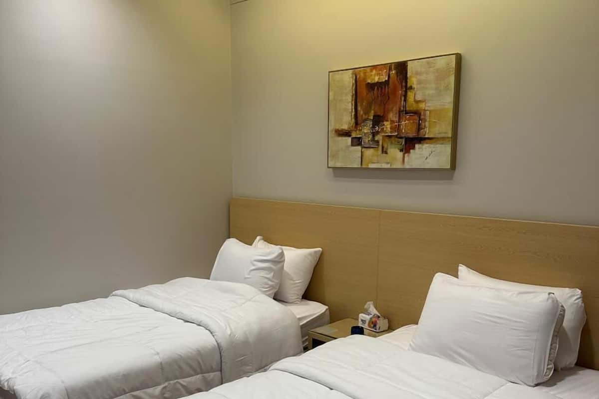Camera d'albergo con due letti, un quadro appeso al muro e una lampada a soffitto.