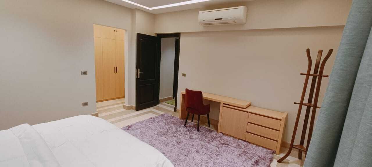A bedroom with a bed, a desk, a chair, a wardrobe, and a coat rack.