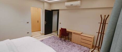 A bedroom with a bed, a desk, a chair, a wardrobe, and a coat rack.