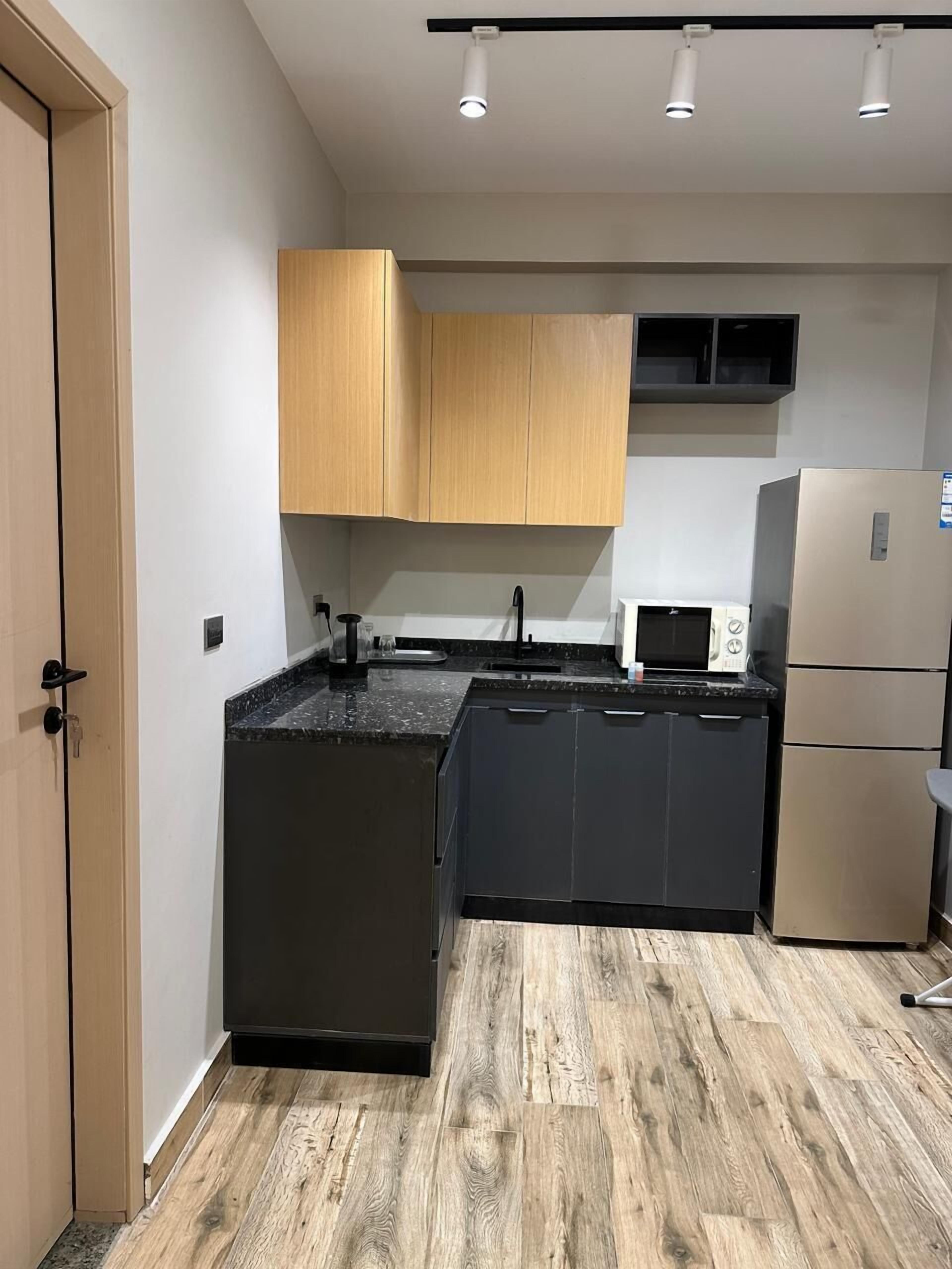 A compact kitchen with dark cabinetry, a built-in microwave, and a stainless steel refrigerator.